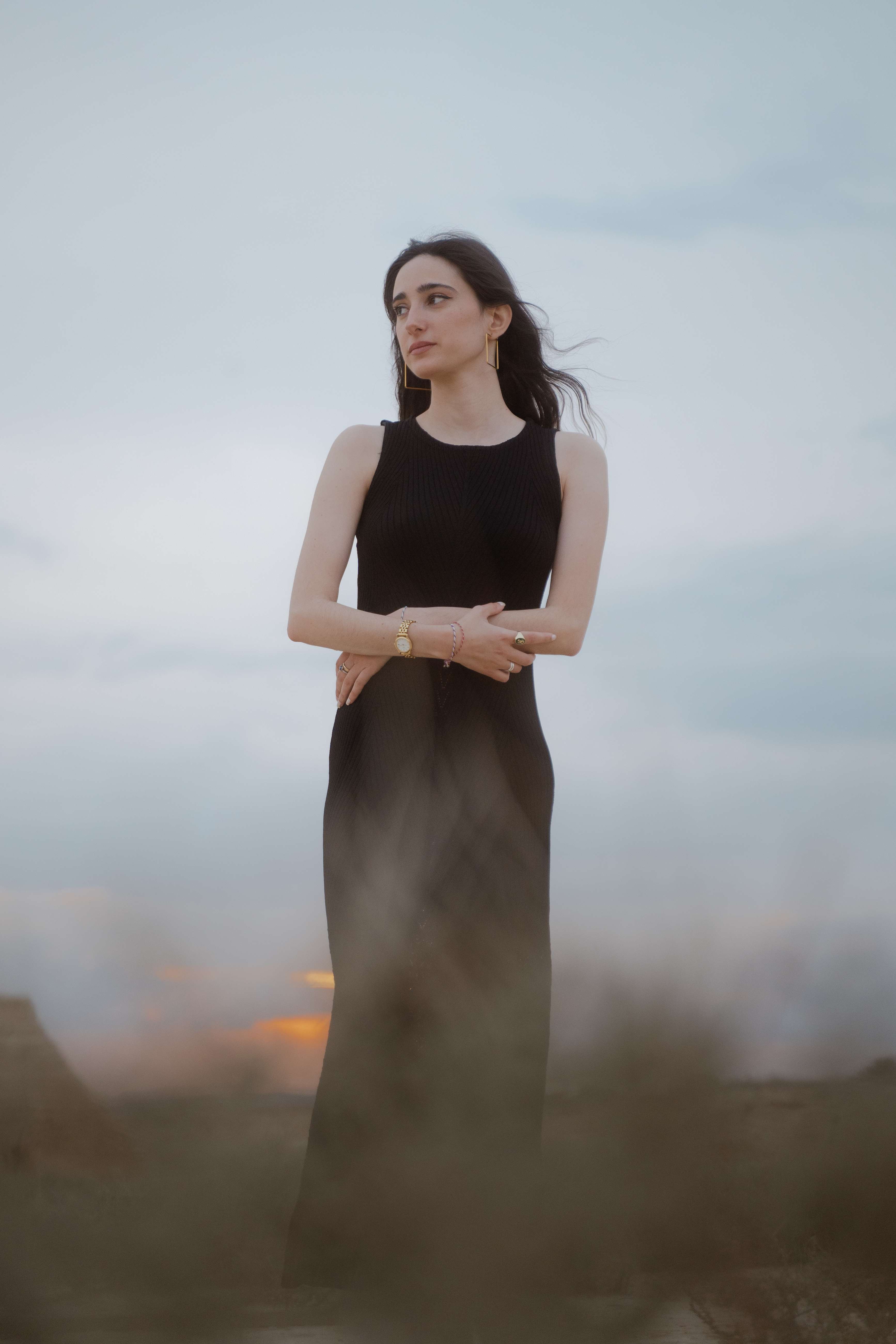 Mujer de vestido negro, manos cruzadas, atardecer dorado
